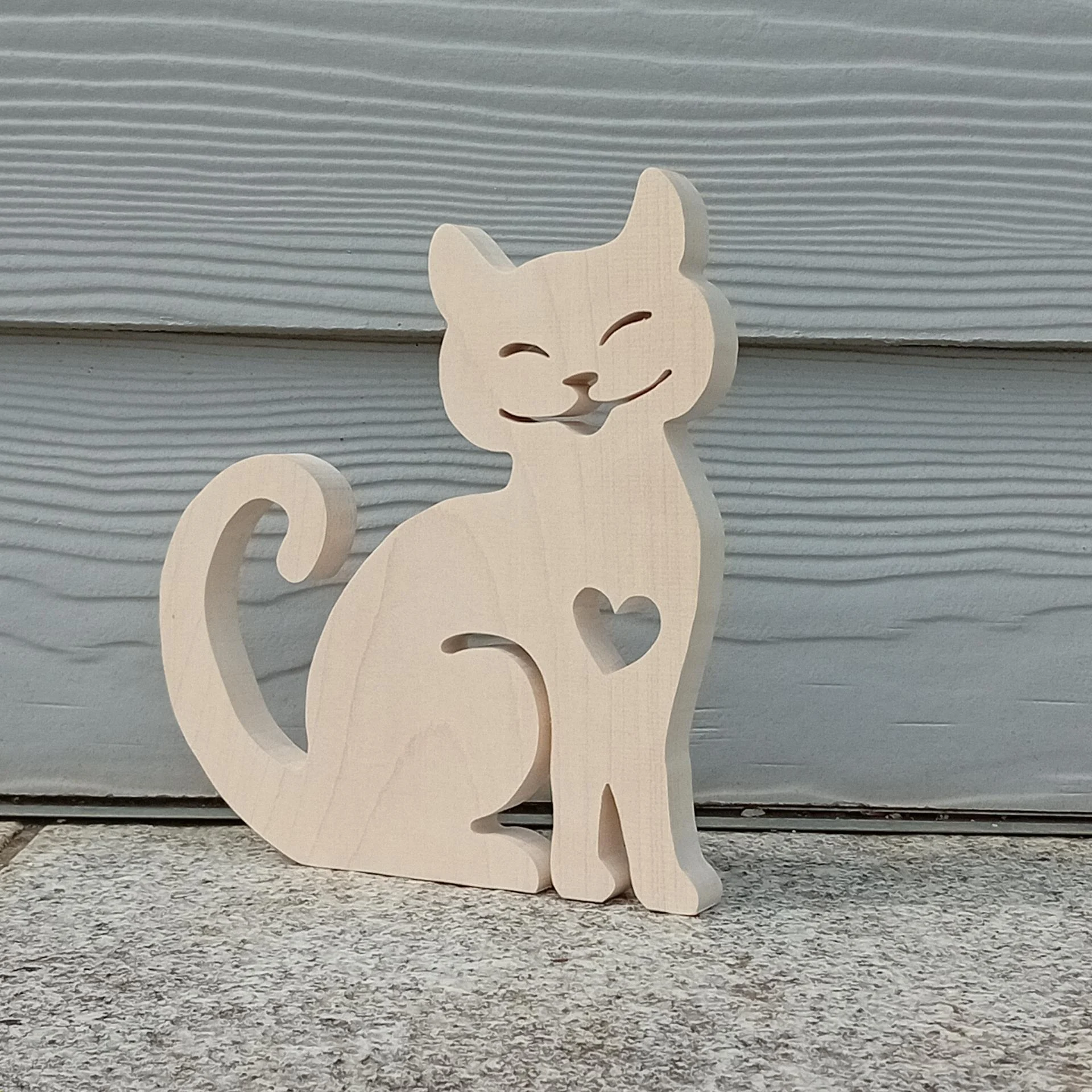 Décoration en bois, découpée à la scie à chantourner, représentant un chat assis avec un coeur découpé sur son poitrail et un lagre sourire.